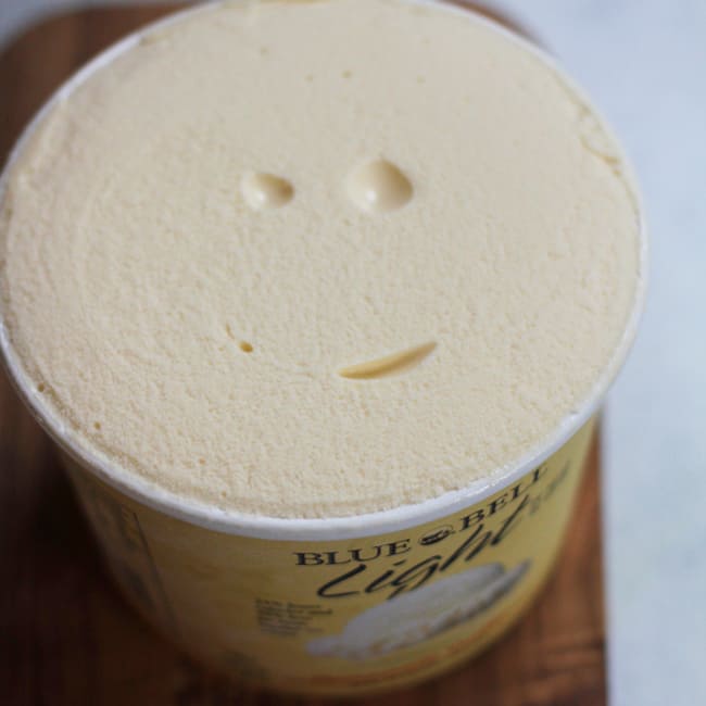 Close-up shot of a half gallon of Blue Bunny light ice cream, with a smiley face on the ice cream.