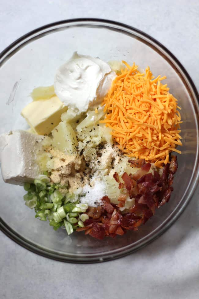 Overhead shot of twice baked potato ingredients, by ingredient in a glass bowl on a white background.