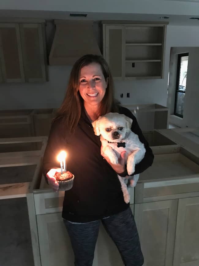 Picture of me holding my shih tzu pup and a chocolate cupcake with 2 candles, in front of my kitchen that is getting remodeled.