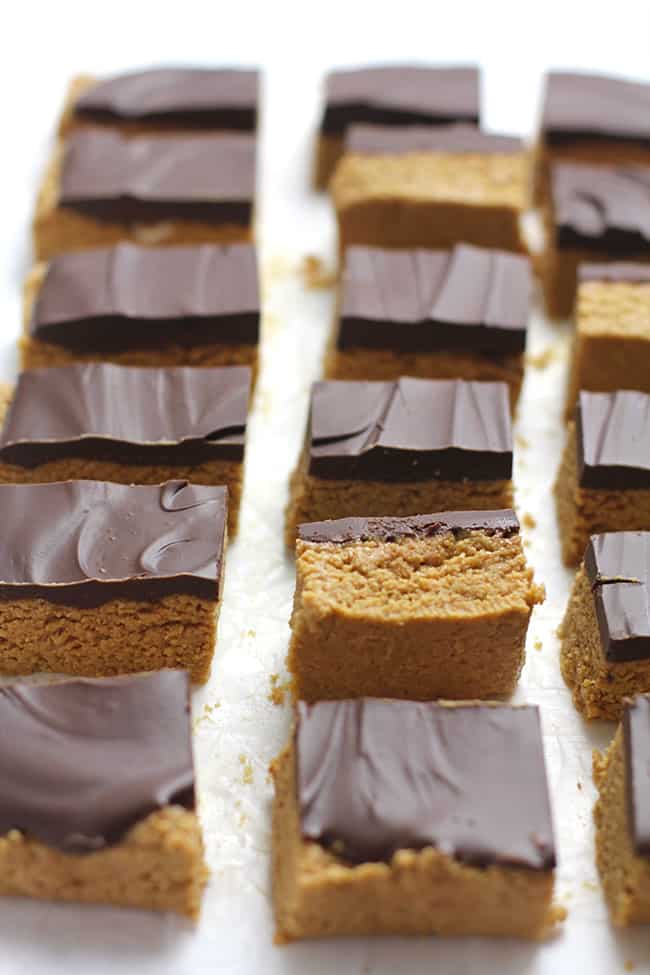 Side shot of a bunch of sliced peanut butter bars, with a few turned on their side, on a white background.
