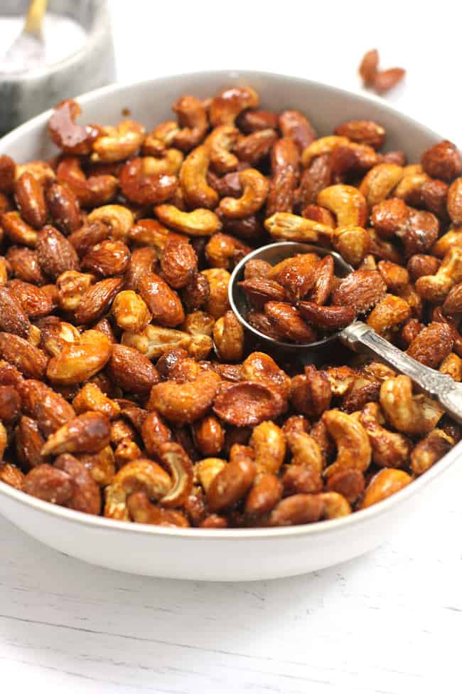 A white bowl of honey roasted nuts with a spoon inside.