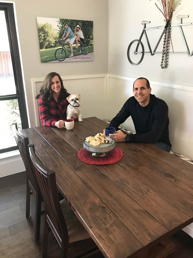 Side shot of me and Mike at the farmhouse table, with Theo on my lap, and coffee mugs in our hands.