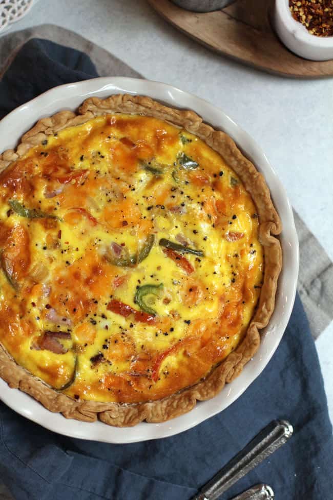 Overhead shot of a ham and cheese quiche in a white pie plate, on a blue napkin.