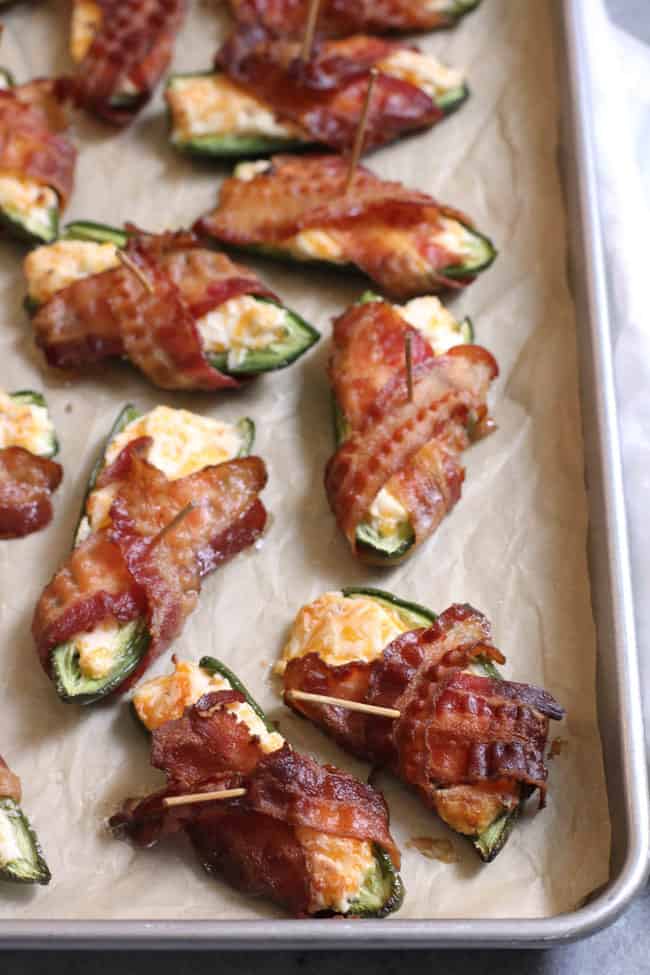 Side shot of bacon wrapped jalapeño poppers on a baking sheet.