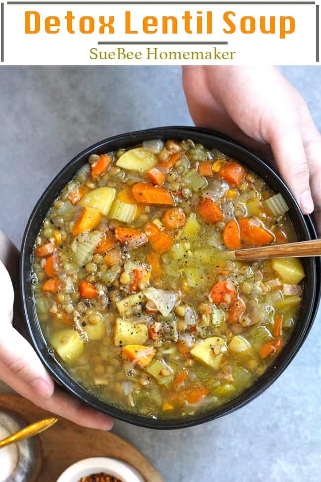 Two hands holding a black bowl of detox lentil soup.
