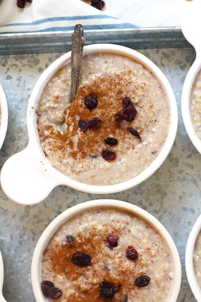 Overhead shot of white bowls of steel cut oats with cinnamon and Craisins, on a gray tray.