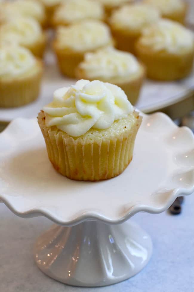 Side shot of one lemon cupcake on a small cake plate, with other cupcakes in the background.