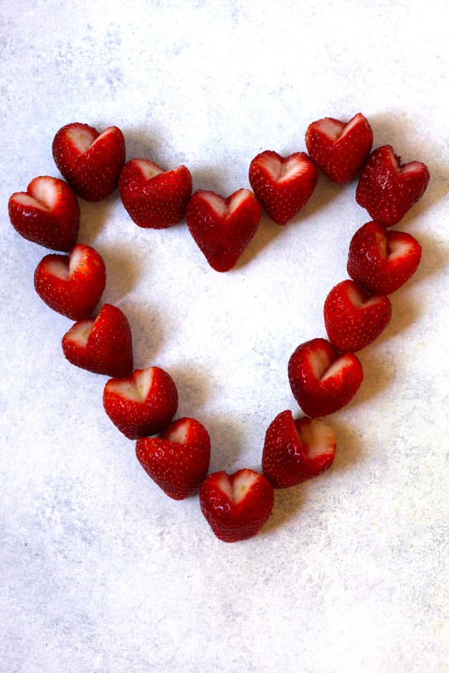 Overhead shot of strawberries cut into hearts, forming a large heart on a white background.