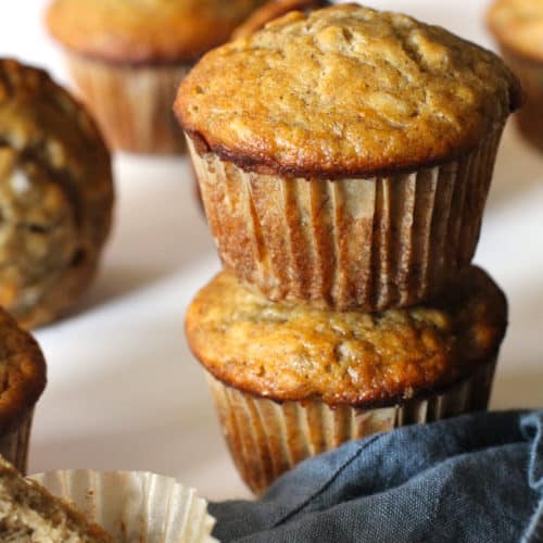 Side shot of stacked banana muffins, with a blue napkin.