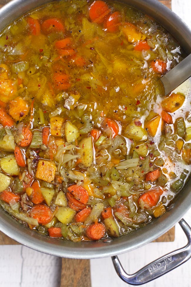 Overhead shot of a large stock pot filled with detox lentil soup, with a soup ladle inside.