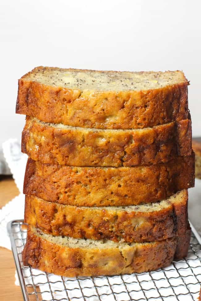 Side shot of a stack of banana bread slices, on a wire rack, with a white napkin.