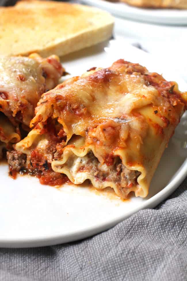 Side shot of a white plate of two lasagna roll ups, on a gray napkin.