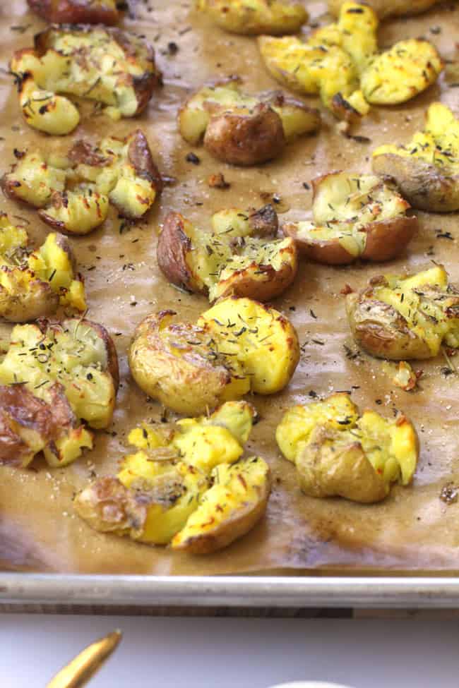 Side shot of a sheet pan of Herb Butter Smashed Potatoes, on tan parchment paper.