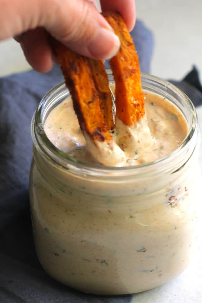 Side shot of my hand dipping Spicy Baked Sweet Potato Fries in a jar of Skinny Chipotle Ranch Dressing.