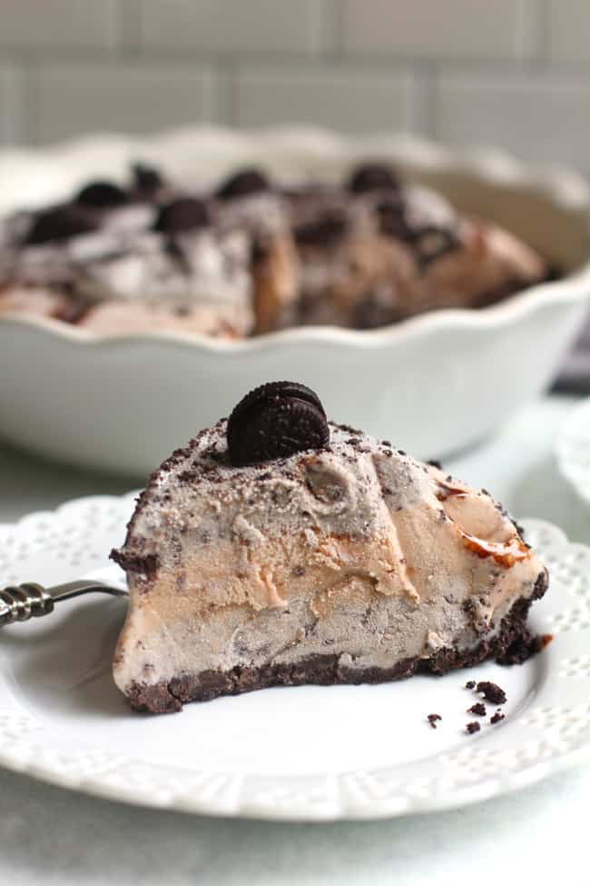 Side shot of one slice of Oreo ice cream pie on a white plate, with the remaining pie in the background.