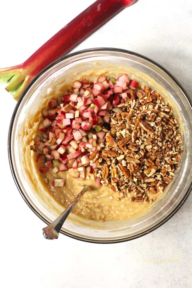 Overhead shot of a glass bowl with rhubarb nut bread ingredients, on a white background.