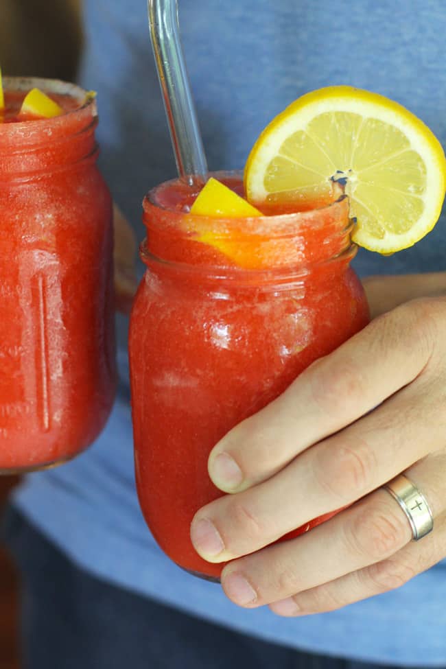 Hands holding two jars of strawberry lemonade vodka slashes.