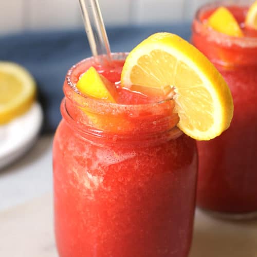 Side shot of two mason jars of strawberry lemonade vodka slushies, with lemon slices and glass straws.