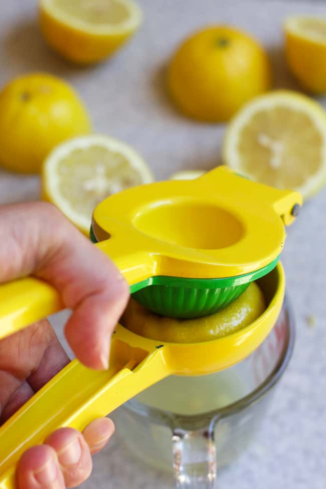 My hand using a citrus press to squeeze lemons into a measuring cup.