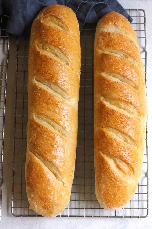 Overhead shot of two large loafs of baked Chewy French bread, on a cooling rack.