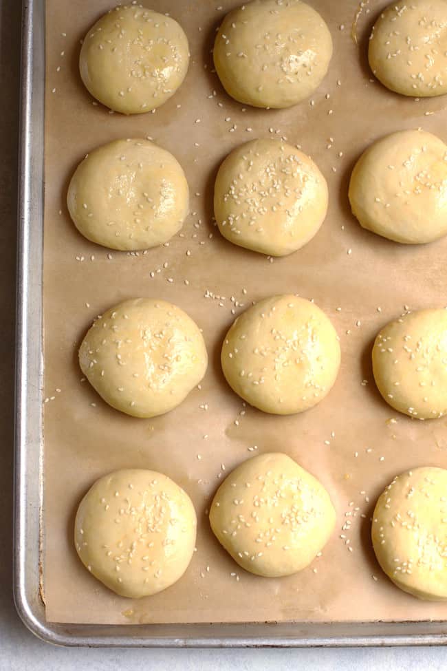 Some brioche hamburger dough mounds on a baking sheet.