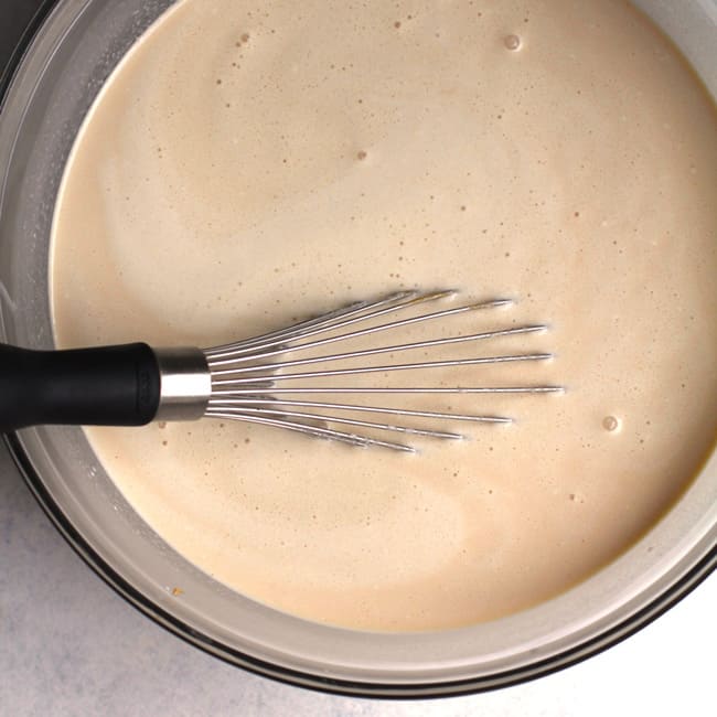 Overhead shot of a large bowl of ice cream mixture in liquid form, with a wire whisk.