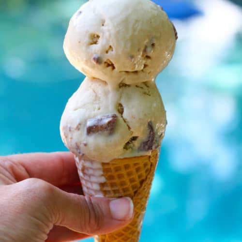 Side view of my hand holding a double dip peanut butter ice cream cone next to a blue pool.