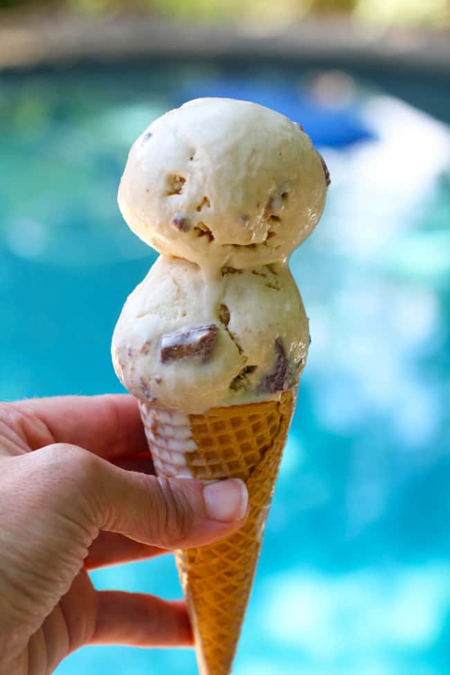 Side view of my hand holding a double dip peanut butter ice cream cone next to a blue pool.