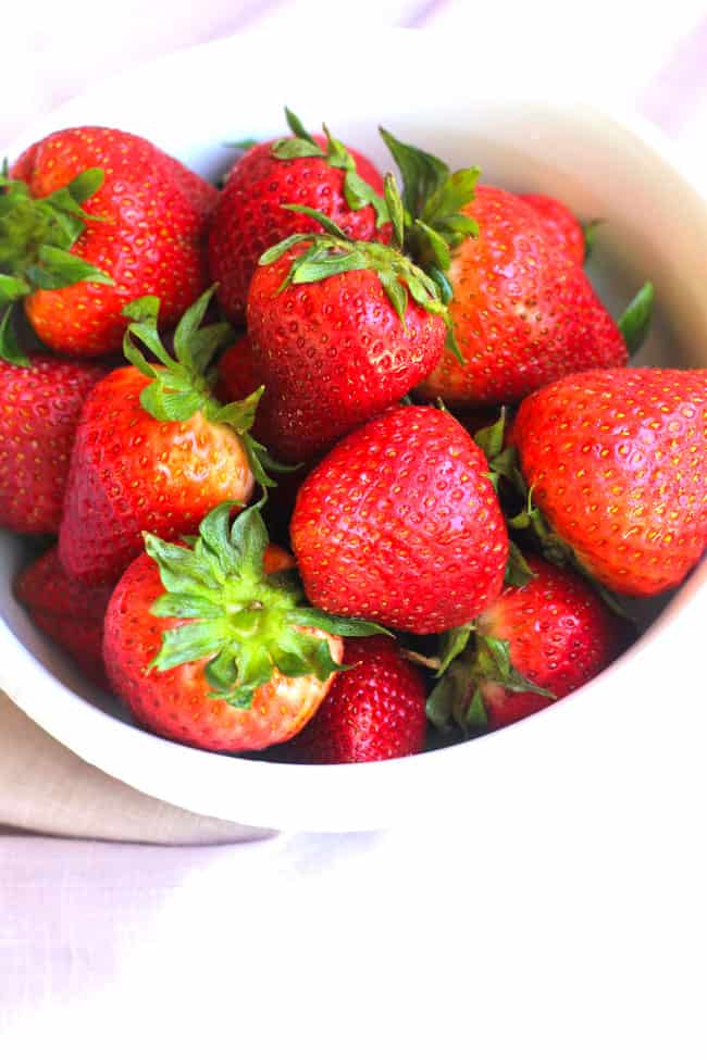 Overhead shot of a bowl of strawberries with stems attached.