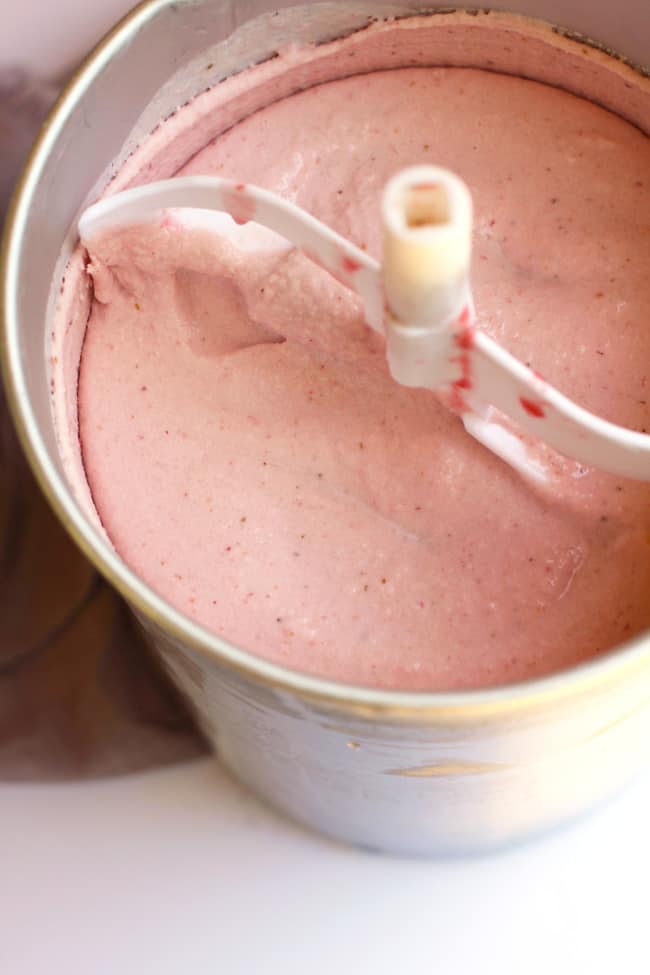 Overhead shot of homemade strawberry ice cream in the canister of a churner, frozen and ready to eat.