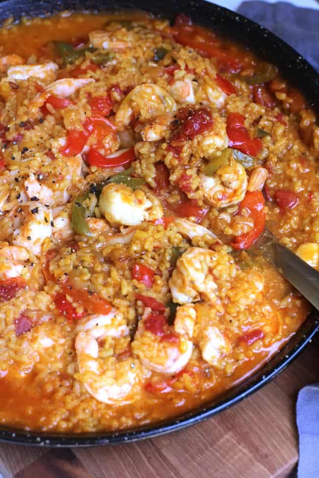 Overhead shot of Spanish Seafood Paella, in a large flat paella pan, with a large serving spoon scooping.