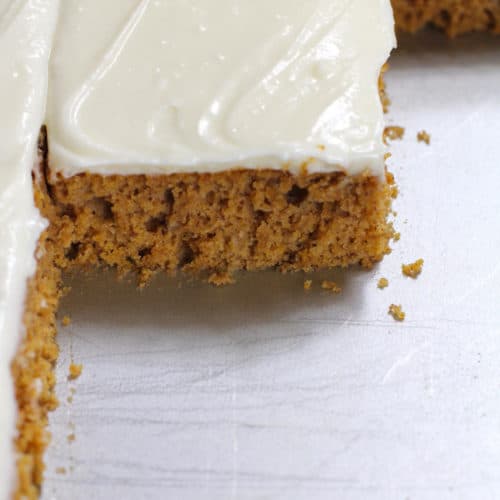 Side shot of a partial pan of pumpkin cake with cream cheese frosting, showing the moist cake layer.