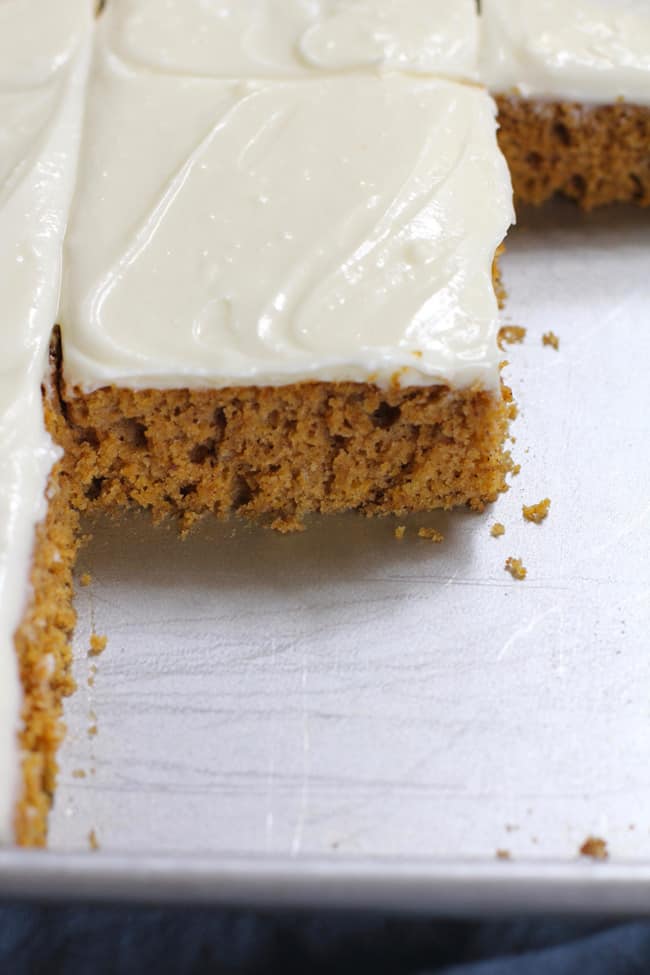 Side shot of a partial pan of pumpkin cake with cream cheese frosting, showing the moist cake layer.