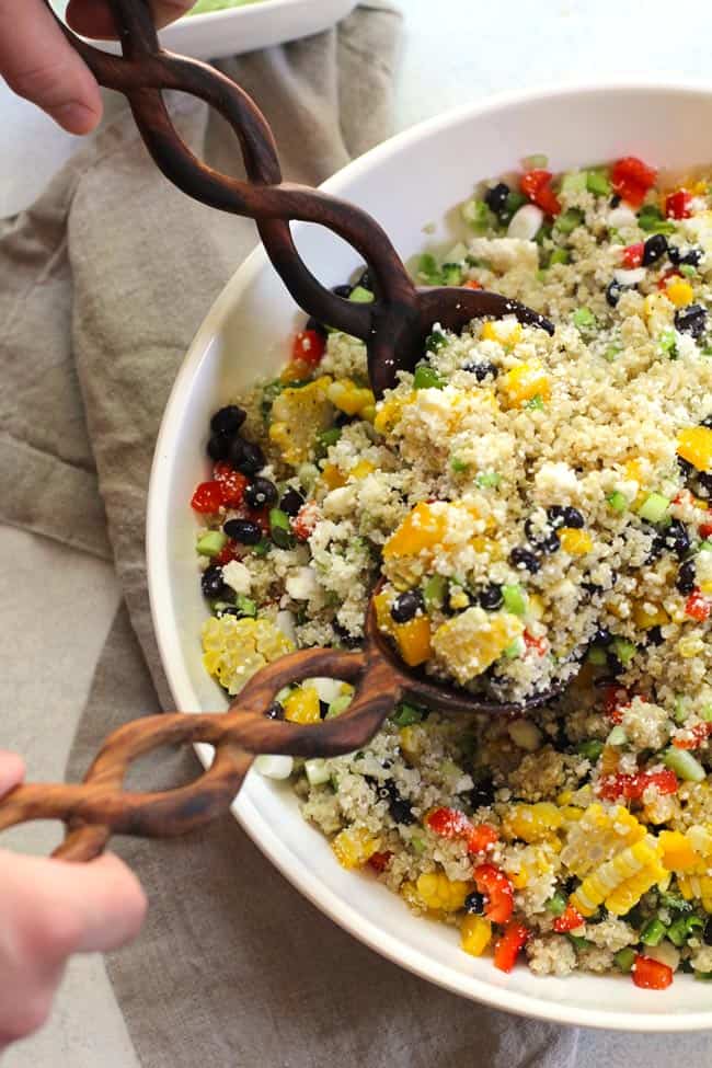 Overhead shot of half of a large white bowl of Mexican Quinoa Salad, with two wooden spoons scooping some up.