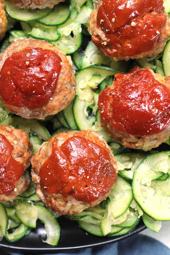 Close up shot of a plate of turkey meatloaf muffins on some zucchini noodles.