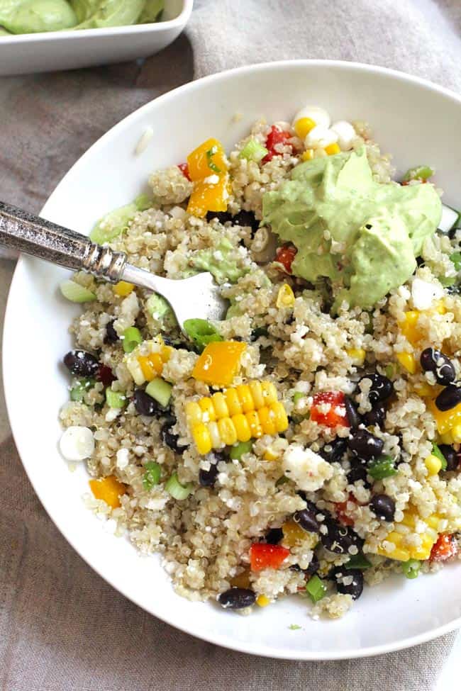 Overhead shot of a white serving bowl of Mexican Quinoa Salad with a dollop of Avocado Crema and a fork.