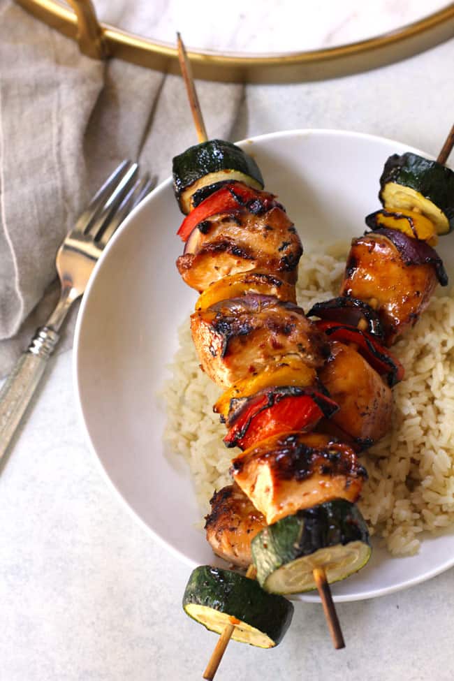 Overhead shot of grilled chicken skewers on a bed of rice in a white bowl.