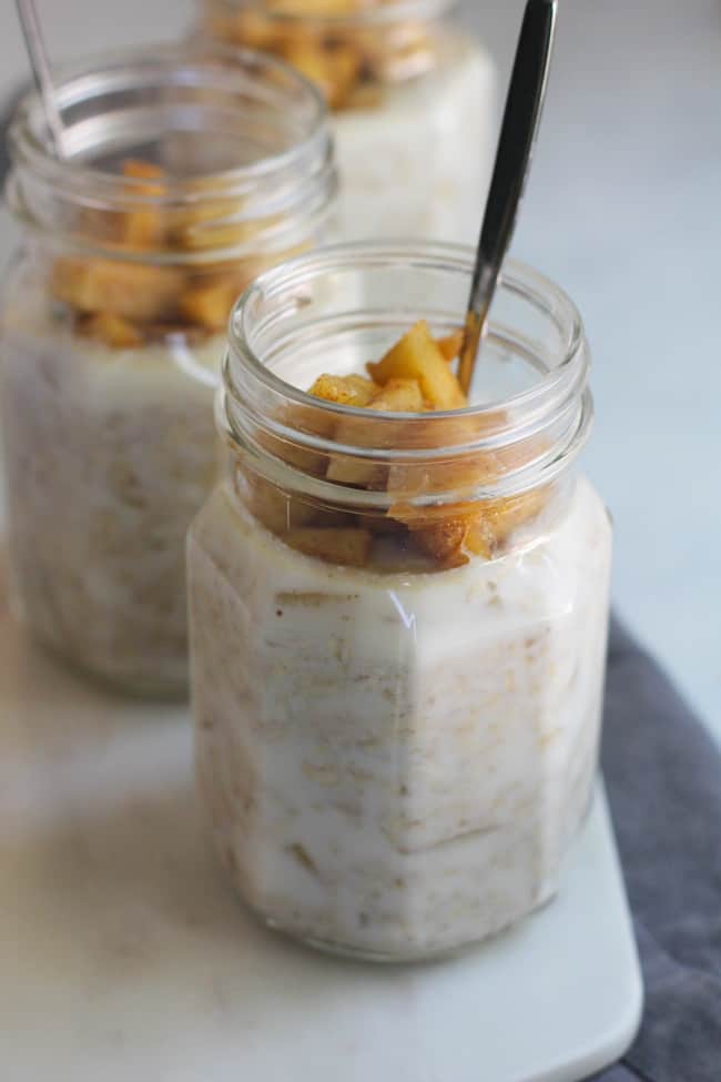 Side shot of three jars of apple pie overnight oats, on a white background.