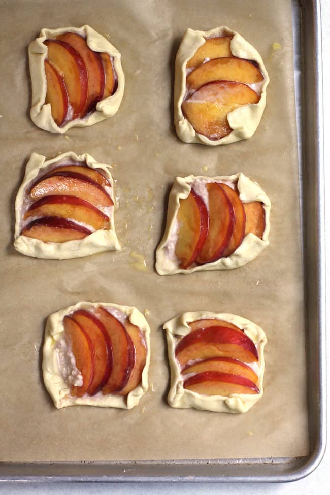 Overhead sheet pan of pre-baked puff pastry peach tartlets.