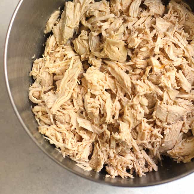 A mixing bowl with shredded chicken breast.