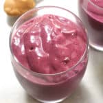 Overhead shot of a berry peanut butter smoothie, in a glass, with a spoonful of peanut butter beside it, on a white background.