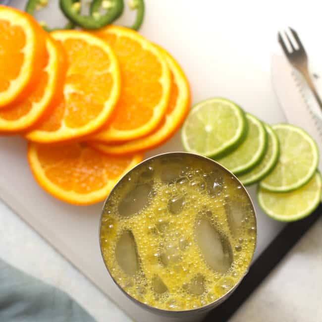 Overhead shot of a cocktail shaker and orange and lime slices.