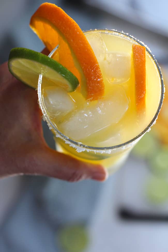 Overhead shot of my hand holding an orange jalapeno margarita, with orange and lime slices.