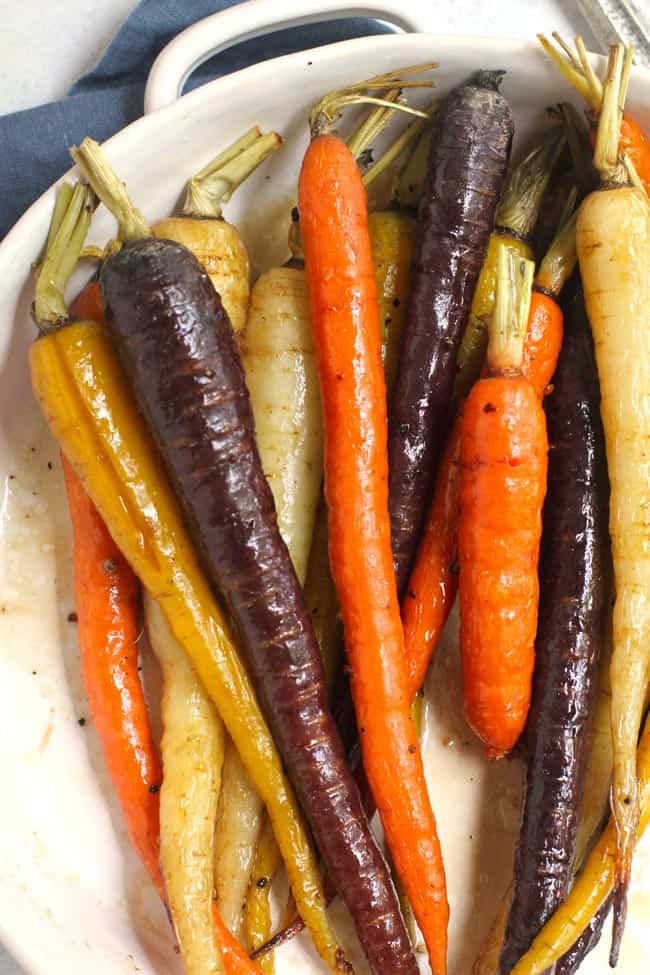 Close-up shot of a round white dish filled with whole multi-colored roasted carrots.
