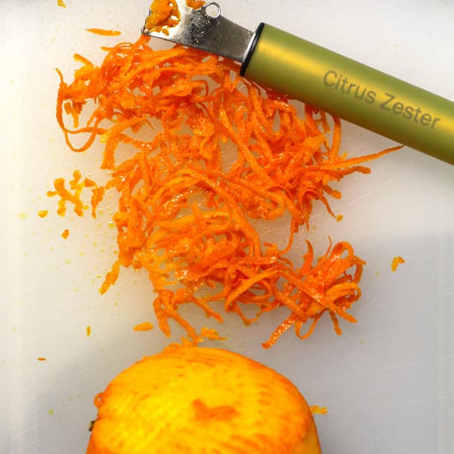 Overhead shot of a orange that has been zested, with orange zest and the zester.