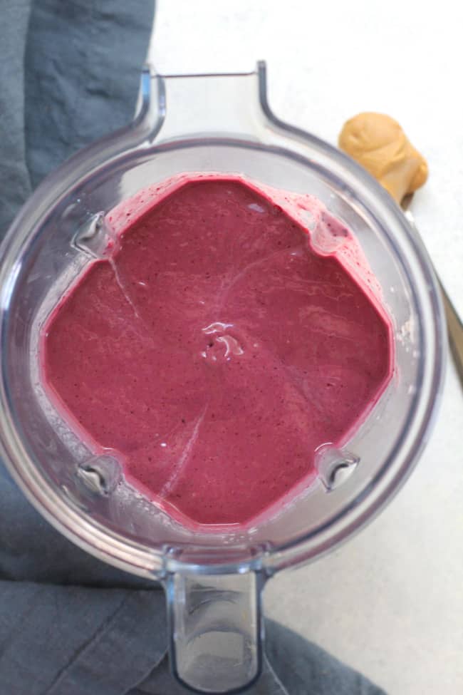 Overhead shot of a vitamix full of berry smoothie, on a white background.