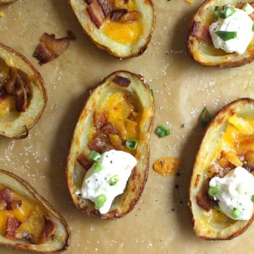 Overhead close-up shot of four crispy potato skins with bacon, cheese, and sour cream.