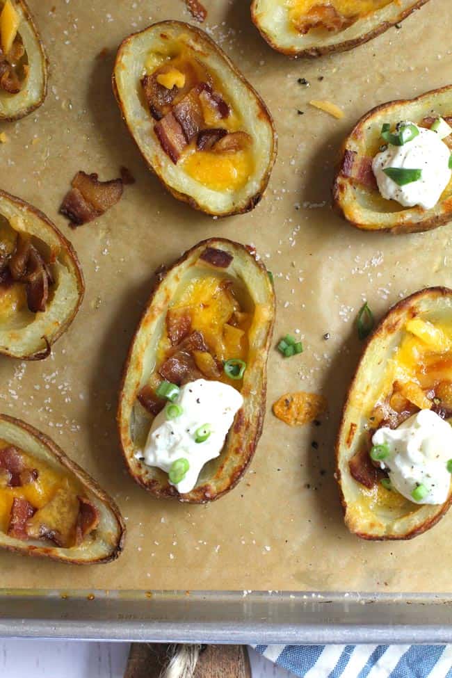 Overhead close-up shot of four crispy potato skins with bacon, cheese, and sour cream.
