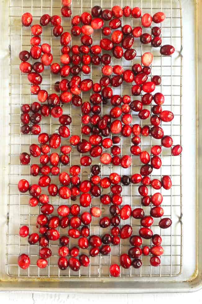 Overhead shot of cranberries spread out on a wire rack inside a baking sheet.