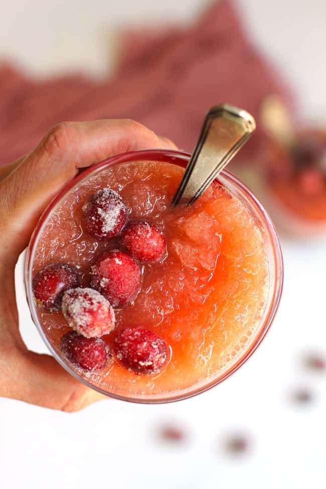 Overhead shot of my hand holding a glass of cranberry slush, with sugared cranberries on top.